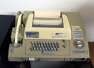 Telex: geschiedenis en werking van een tekstnet ASR 32-telexmachine met een toetsenbord van drie rijen en vijfkanaals ponsband voor het vastleggen en verzenden van tekst.